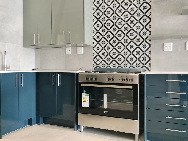 Modern kitchen featuring high-gloss blue cabinetry, stone countertops, a patterned tile splashback, and a stainless steel freestanding oven.