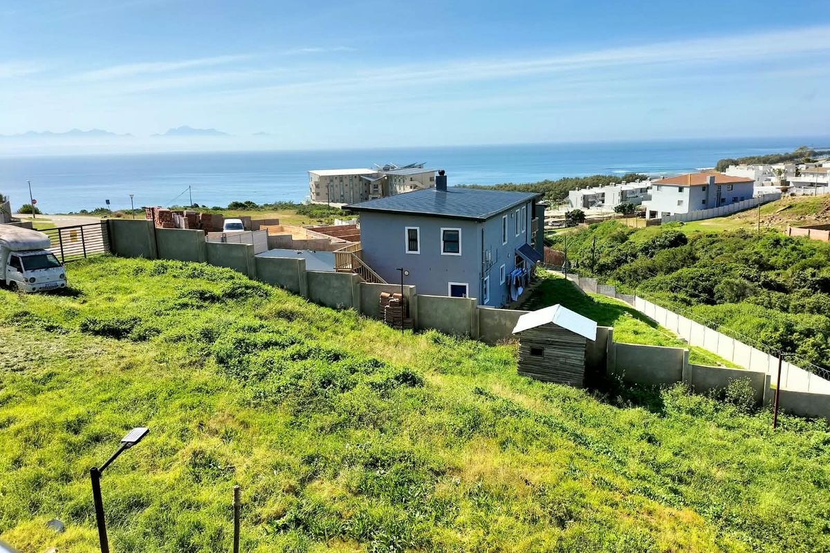 Aerial view of a vacant residential plot featuring a perimeter wall, a small wooden shed, and expansive ocean views.
