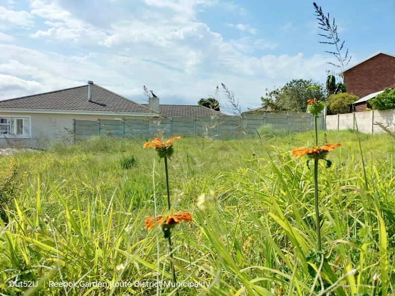 A vacant residential plot featuring overgrown grass and a precast concrete boundary wall, situated in a established neighborhood.