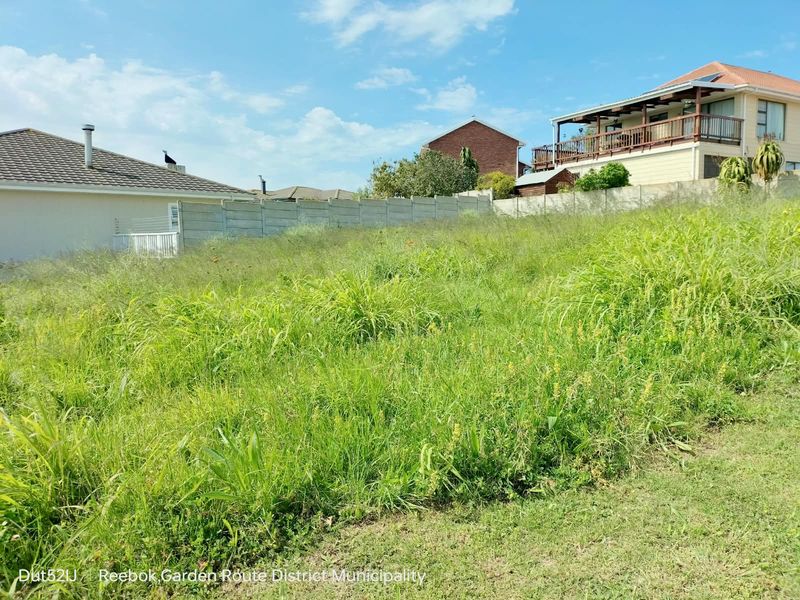 A vacant residential plot featuring overgrown grass and a precast concrete boundary wall, situated in a developed neighborhood.
