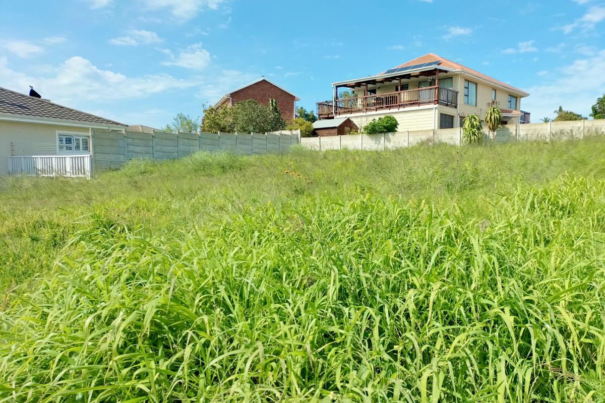 A vacant residential plot featuring a sloped grassy terrain enclosed by precast concrete boundary walls, situated in a developed neighborhood.