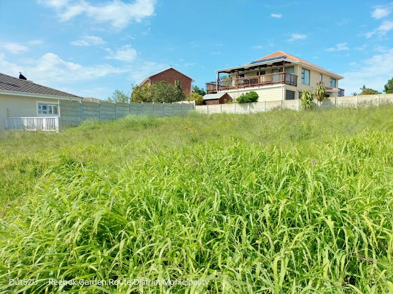 A vacant residential plot featuring a sloped grassy terrain enclosed by precast concrete boundary walls, situated in a developed neighborhood.