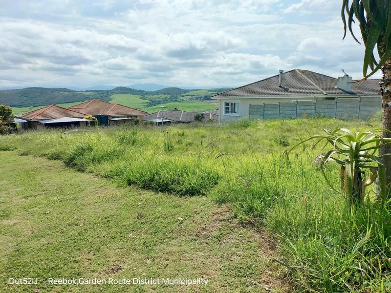 A view of a vacant residential plot featuring natural grass coverage with surrounding neighborhood homes and distant mountain landscape views.