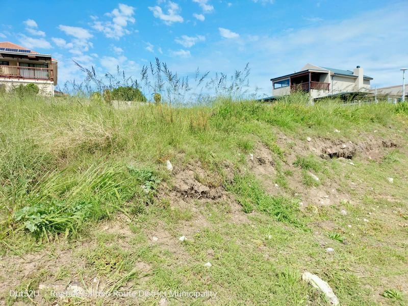 A sloped vacant residential plot featuring natural vegetation and surrounding neighborhood homes, offering potential for development.