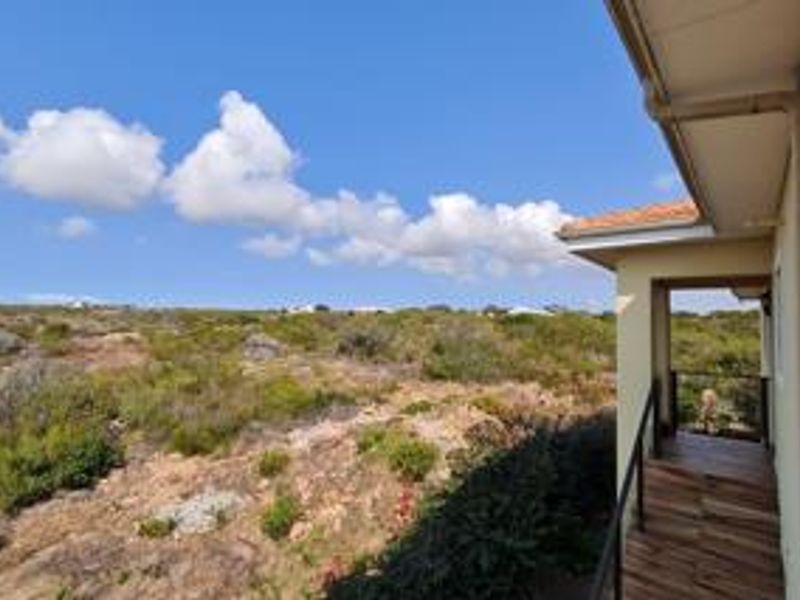 A covered balcony featuring tiled flooring and metal railings, offering an expansive view of the surrounding natural landscape.