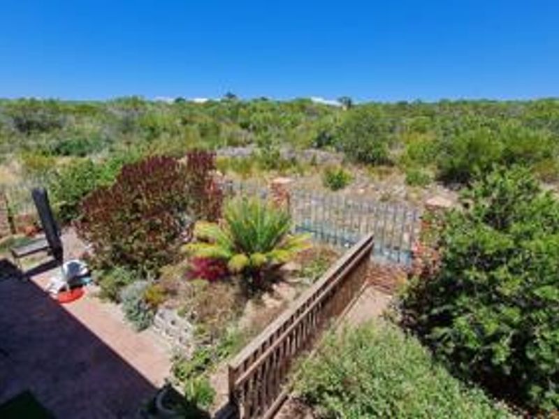 A rear outdoor area featuring brick paving, a landscaped garden with established shrubs, and a combination of brick and metal boundary fencing.