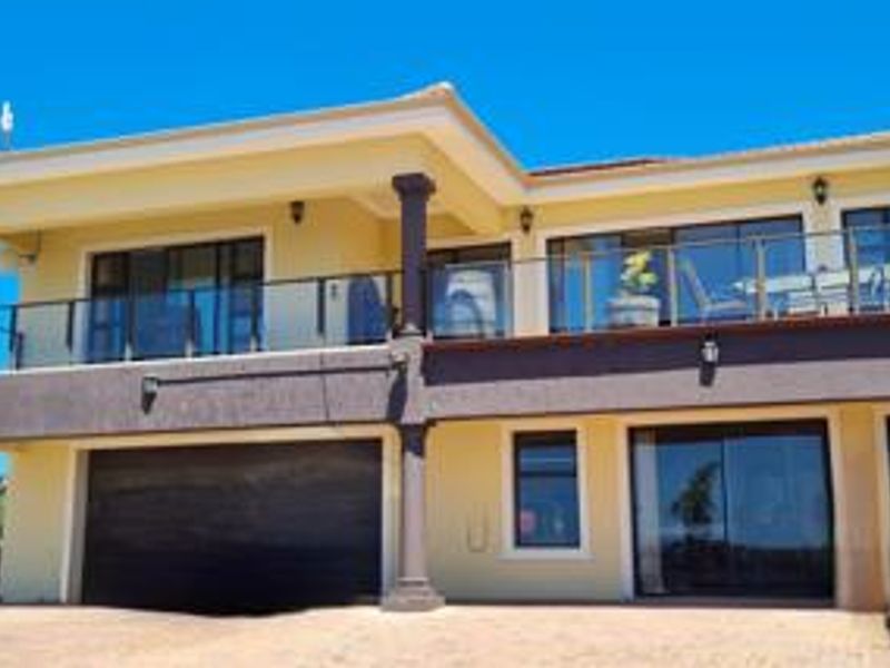 A two-story residential facade featuring a spacious upper balcony with glass balustrades, a ground-level garage, and modern sliding door access.