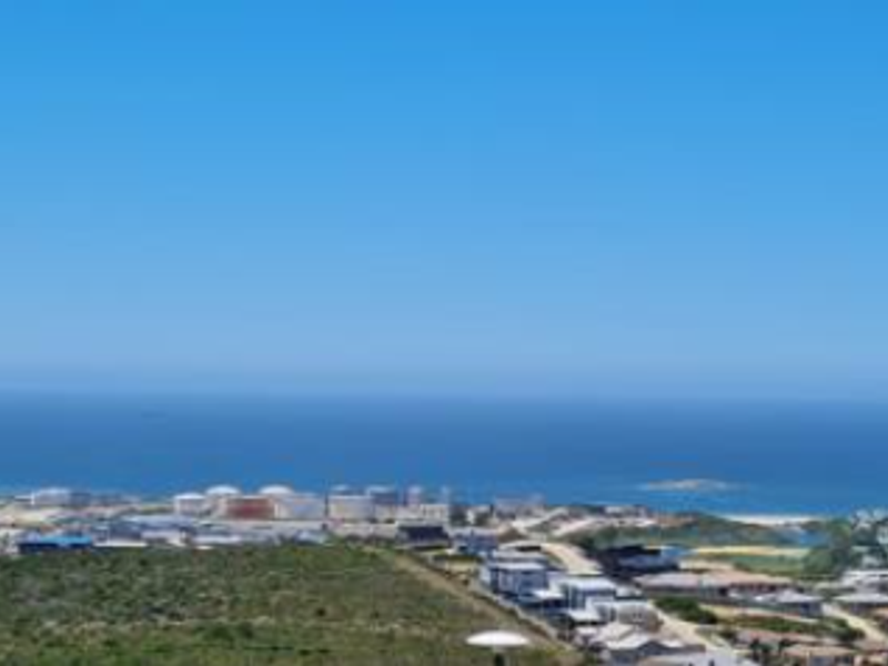 A wide-angle elevated view overlooking the coastal landscape, residential area, and the ocean horizon.