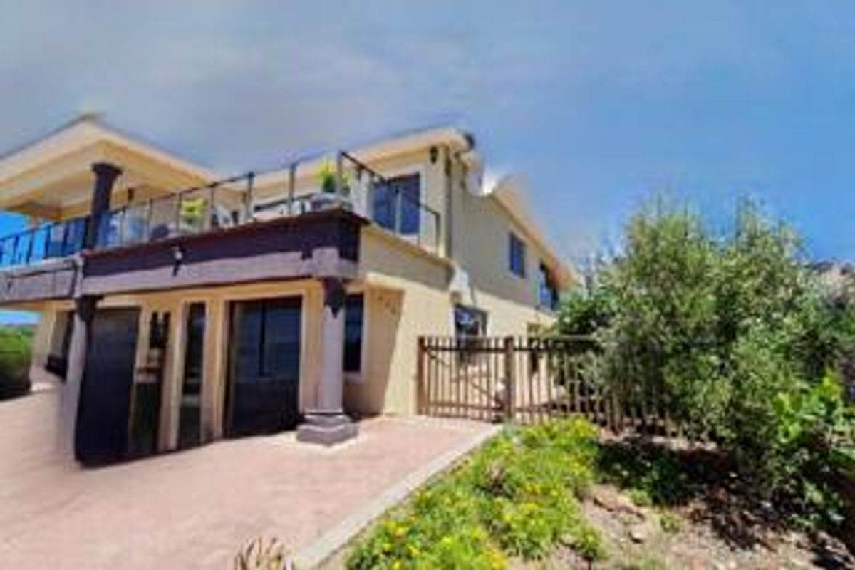 Rear view of the property featuring a paved patio area, a raised balcony with glass balustrades, and a timber fence bordering the garden.