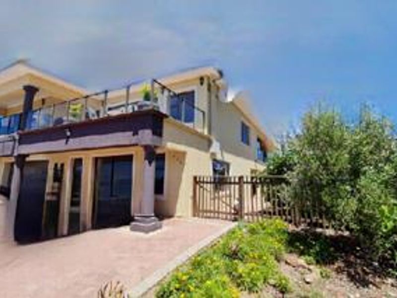 Rear view of the property featuring a paved patio area, a raised balcony with glass balustrades, and a timber fence bordering the garden.