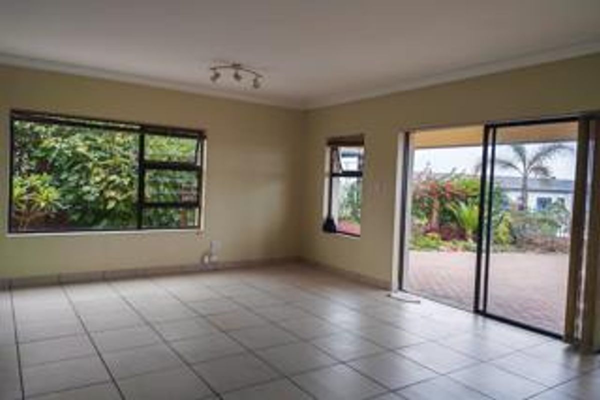 A spacious, empty living room featuring neutral tiled flooring, large windows, and sliding glass doors that provide direct access to the outdoor patio area.