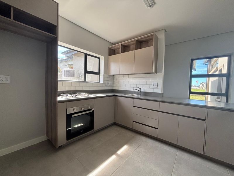 Modern kitchen featuring neutral-toned cabinetry, stone countertops, subway tile backsplash, integrated gas hob, and built-in oven in a clean, contemporary layout.
