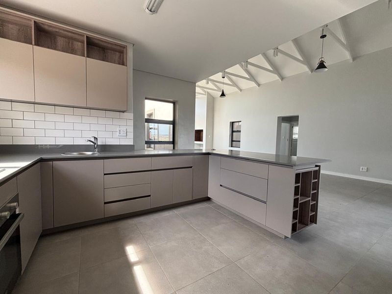 Modern open-plan kitchen featuring sleek cabinetry, stone countertops, subway tile backsplash, and exposed roof trusses in a bright, spacious living area.