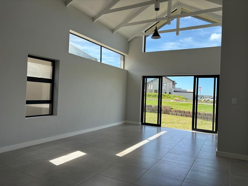Spacious, light-filled living area featuring high vaulted ceilings with exposed trusses, large sliding doors to the garden, and modern tiled flooring.