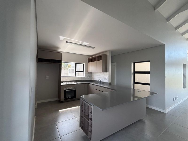 Modern kitchen featuring stone countertops, a central island, built-in oven, gas hob, and subway tile backsplash in a clean, neutral space.