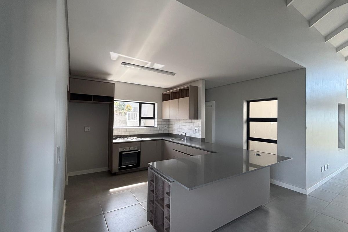Modern kitchen featuring stone countertops, a central island, built-in oven, gas hob, and subway tile backsplash in a clean, neutral space.