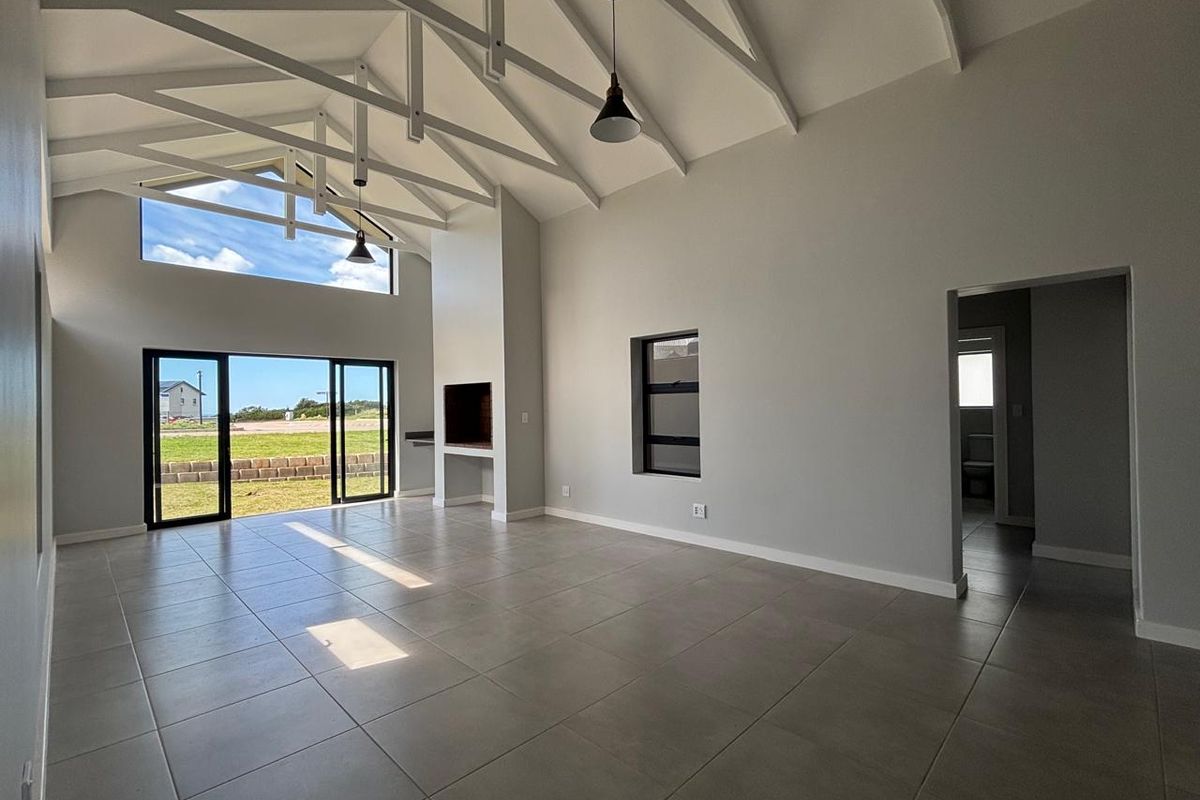 Spacious open-plan living area featuring high vaulted ceilings with exposed trusses, tiled floors, a built-in fireplace, and large sliding doors leading to the garden.