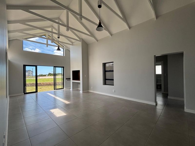Spacious open-plan living area featuring high vaulted ceilings with exposed trusses, tiled floors, a built-in fireplace, and large sliding doors leading to the garden.