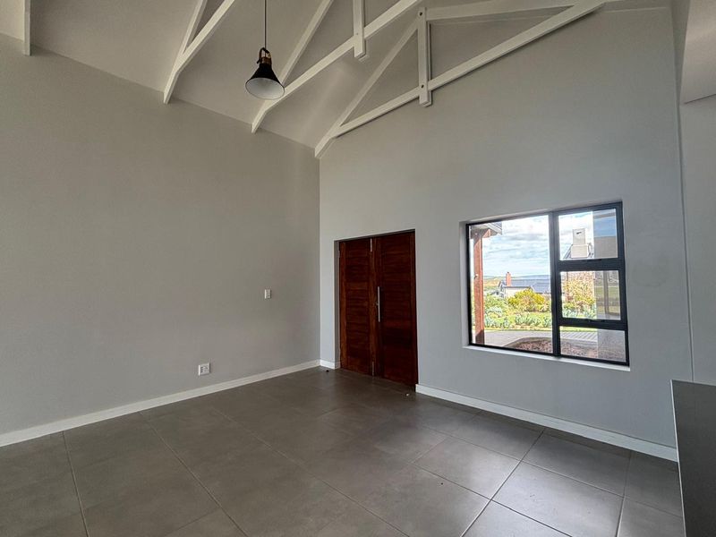 Spacious living area featuring high vaulted ceilings with exposed trusses, large windows, tiled flooring, and double timber doors leading to the exterior.