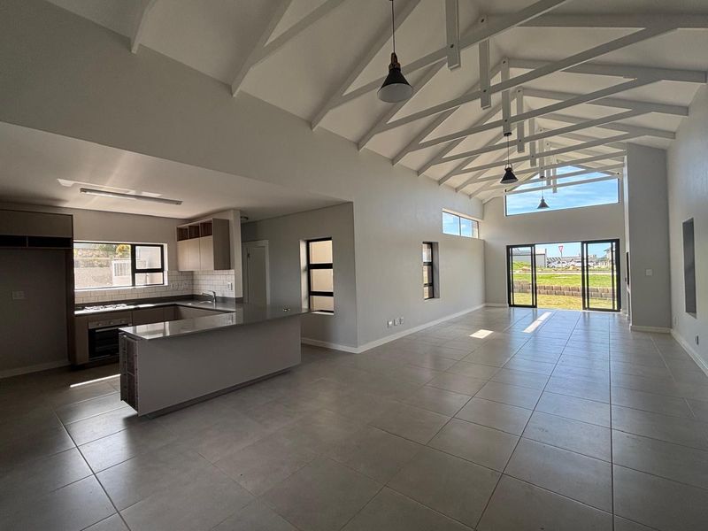 Spacious open-plan living area featuring a high vaulted ceiling with exposed trusses, tiled floors, and a modern kitchen with stone countertops and built-in appliances.