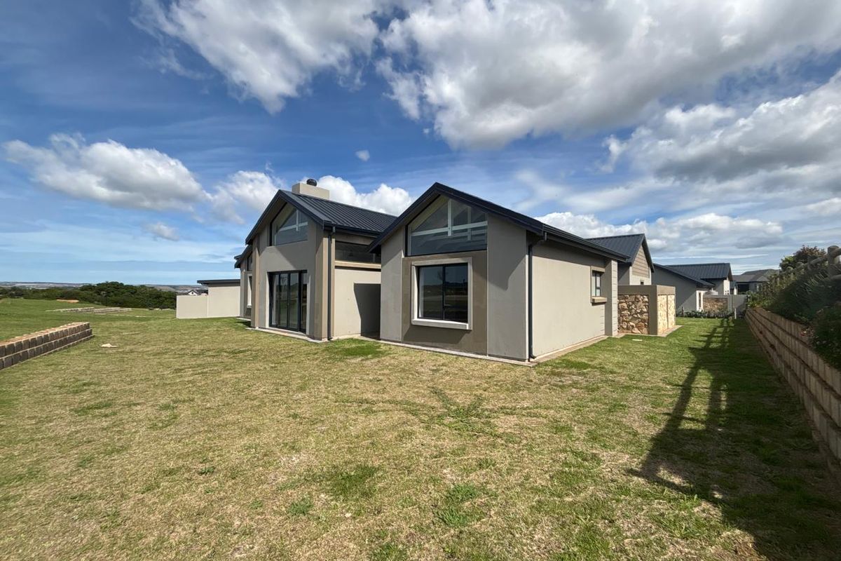 Rear view of a modern house featuring pitched roofs, stone cladding, and large windows overlooking a spacious lawn.