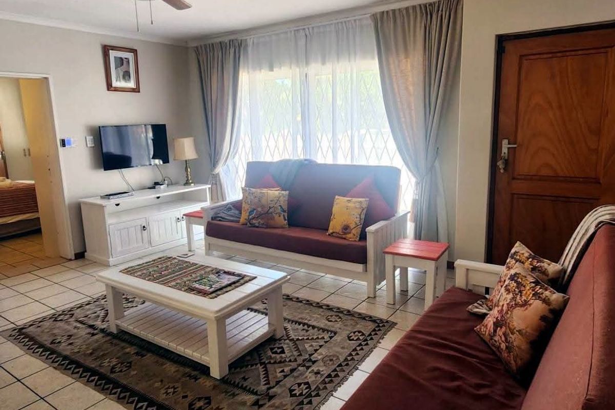 A comfortable living room featuring tiled flooring, a ceiling fan, and natural light through large windows with curtains.