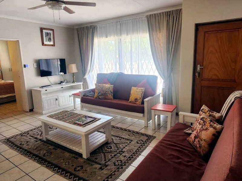 A comfortable living room featuring tiled flooring, a ceiling fan, and natural light through large windows with curtains.