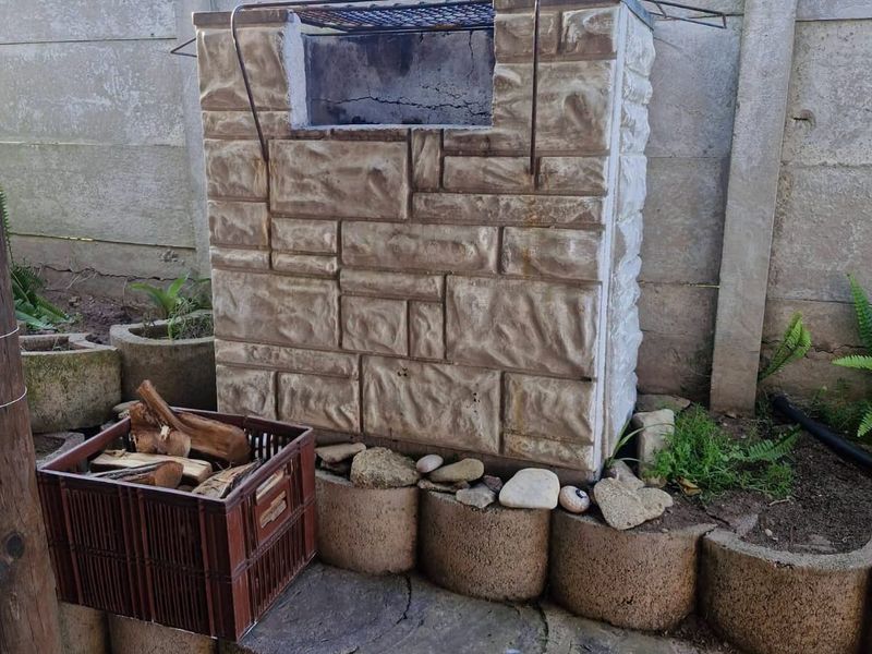 Outdoor area featuring a built-in stone-clad braai unit set against a precast concrete boundary wall with tiered concrete retaining blocks.
