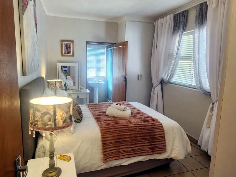 A cozy bedroom featuring tiled flooring, built-in cupboards, and an en-suite pedestal basin area with window blinds for privacy.