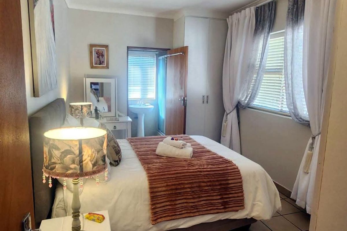 A cozy bedroom featuring tiled flooring, built-in cupboards, and an en-suite pedestal basin area with window blinds for privacy.