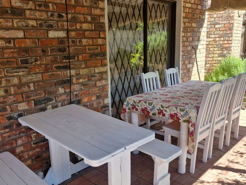 A covered outdoor patio area featuring exposed brick walls, paved flooring, and a timber pergola structure, providing a functional space for outdoor dining.
