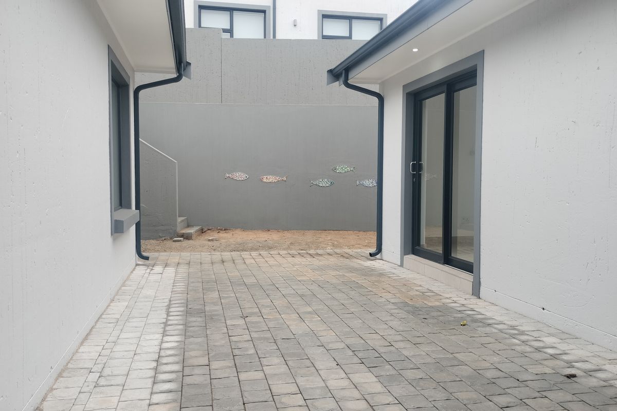 A paved rear courtyard area featuring a sliding glass door entrance and a retaining wall with decorative fish accents.