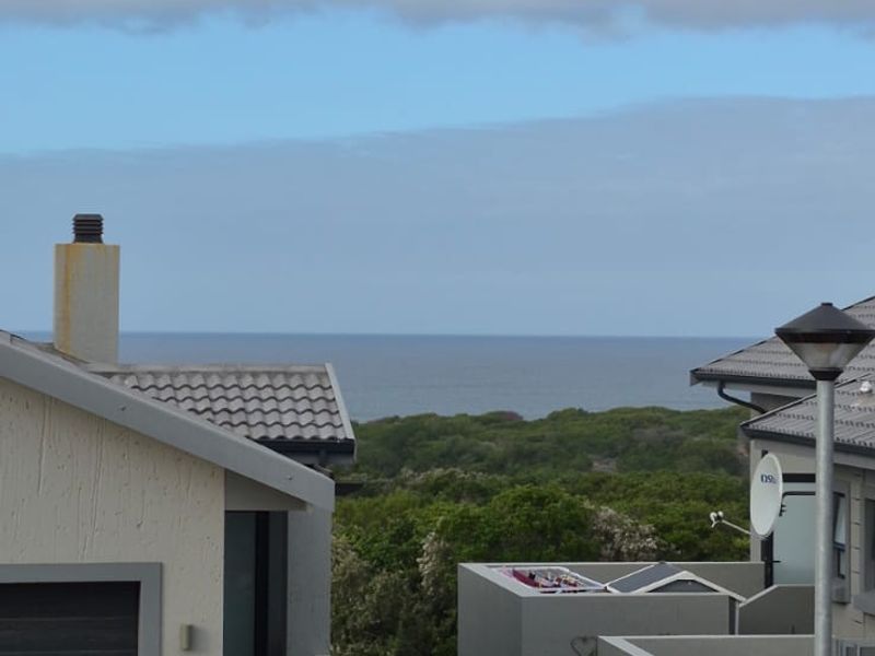 Front exterior view of a modern residence featuring a paved driveway, garage, and landscaped garden with a scenic ocean view in the background.