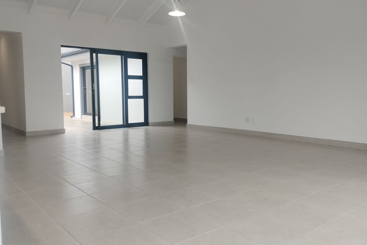 Spacious, empty living area featuring neutral tiled flooring, vaulted ceilings, and large sliding glass doors providing access to the exterior.