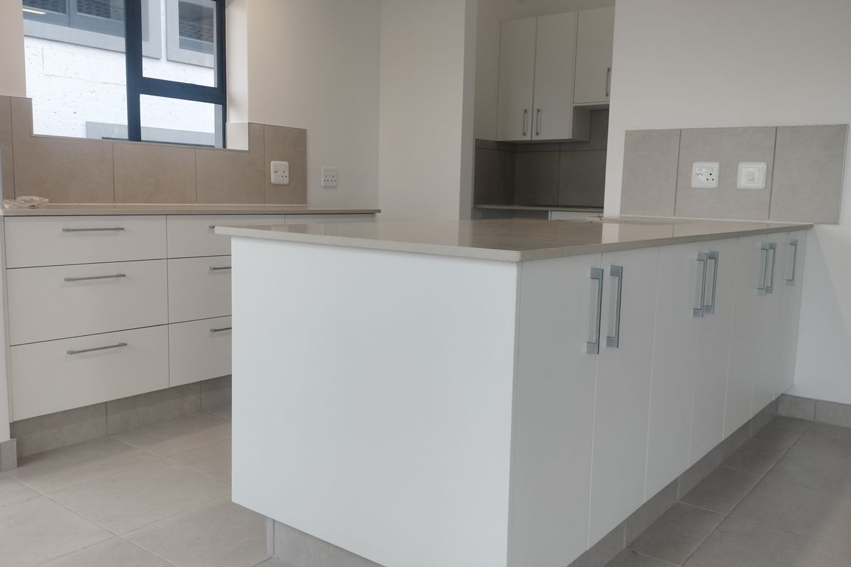 A modern, clean-lined kitchen featuring a central island, white cabinetry, stone countertops, and neutral tiled flooring in an open-plan layout.