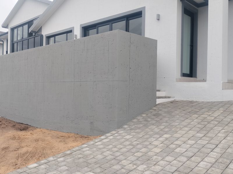 Modern front facade featuring a prominent concrete retaining wall, paved driveway, and tiled entrance steps, with surrounding landscaping currently in progress.