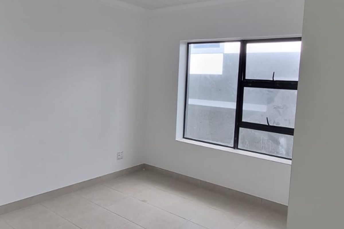 A bright, empty bedroom featuring neutral tiled flooring, a white tongue and groove ceiling with recessed lighting, and a modern aluminium window.
