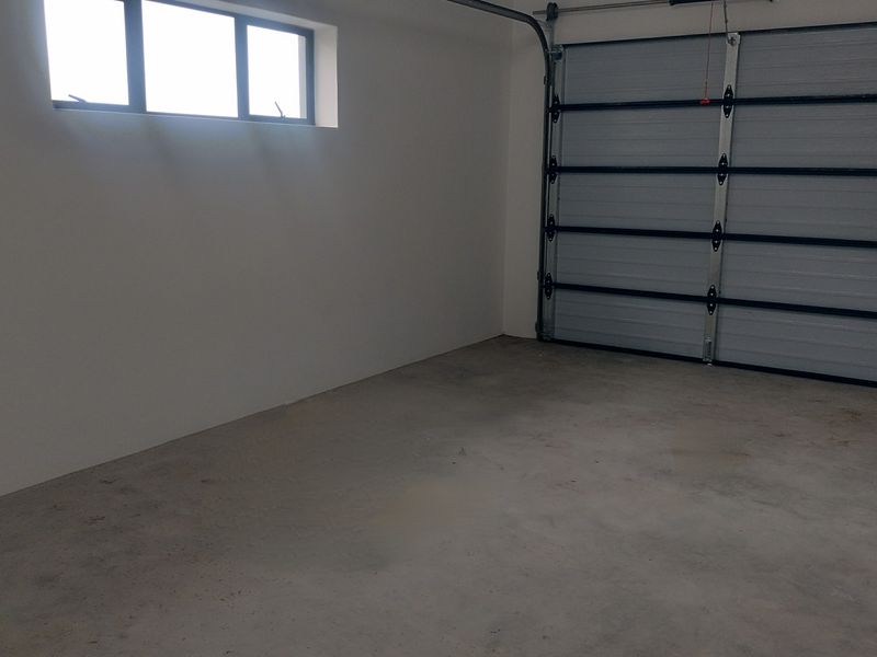 A clean, empty garage space featuring a sectional garage door, concrete flooring, and a high-level window for natural light.