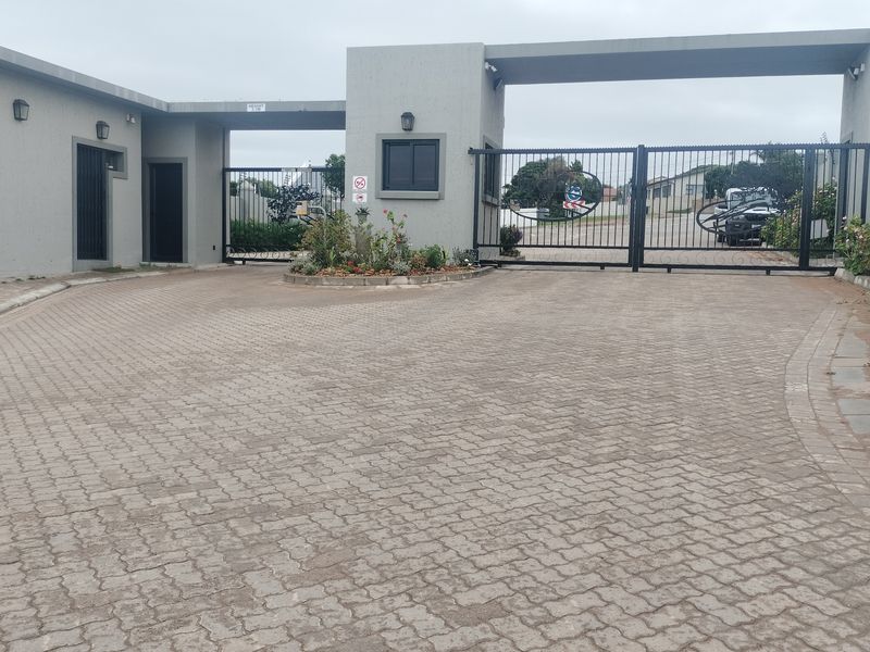 A secure gated entrance to the property featuring a paved driveway, modern gate house structure, and established garden beds.