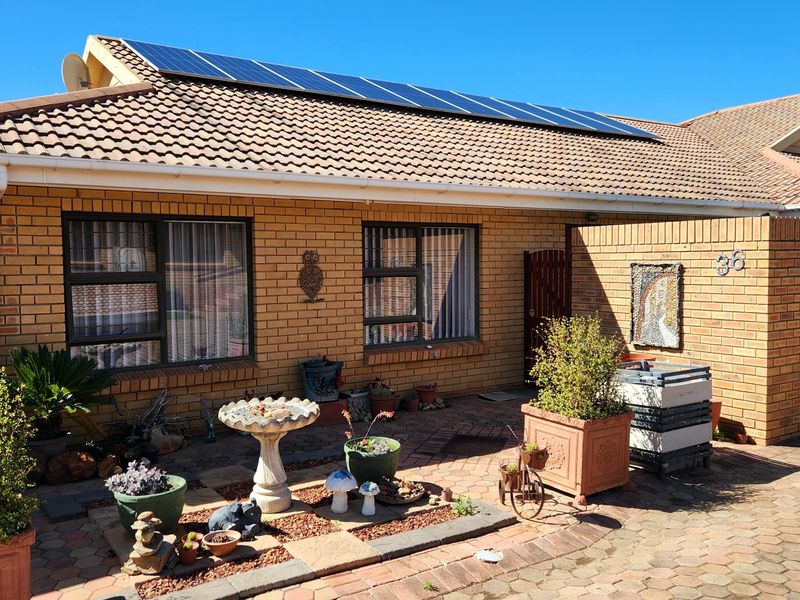 Front elevation of a facebrick house featuring a tiled roof with integrated solar panels and a paved entrance area.