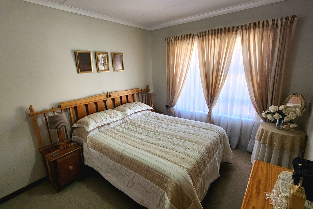 A well-maintained bedroom featuring neutral wall tones, carpeted flooring, and large windows with fitted curtain tracks.