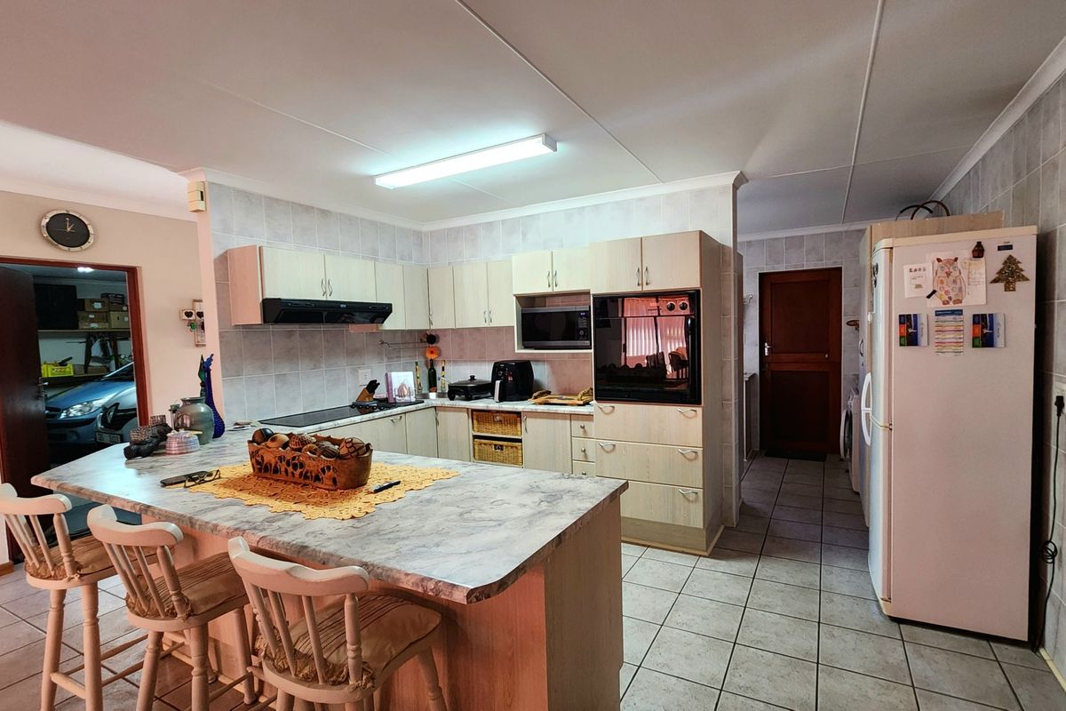 A functional kitchen featuring light wood cabinetry, a central island with breakfast bar seating, tiled flooring, and integrated oven and extractor fan.