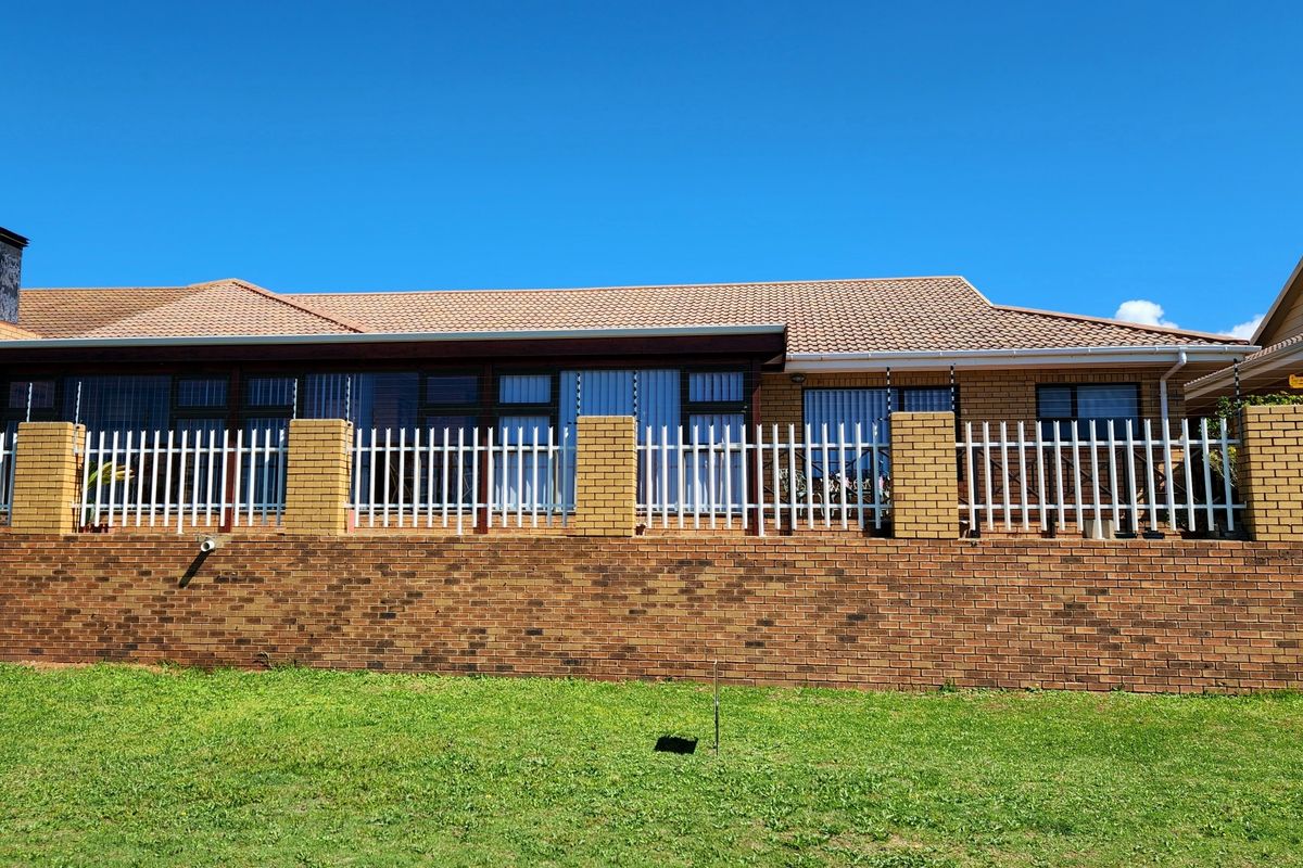 Rear view of the house featuring a brick retaining wall, white metal fencing, and a tiled roof with sliding glass door access.