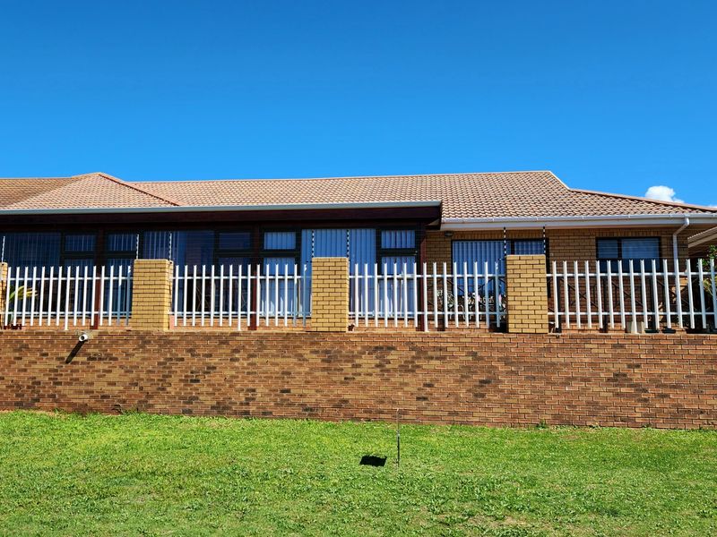 Rear view of the house featuring a brick retaining wall, white metal fencing, and a tiled roof with sliding glass door access.