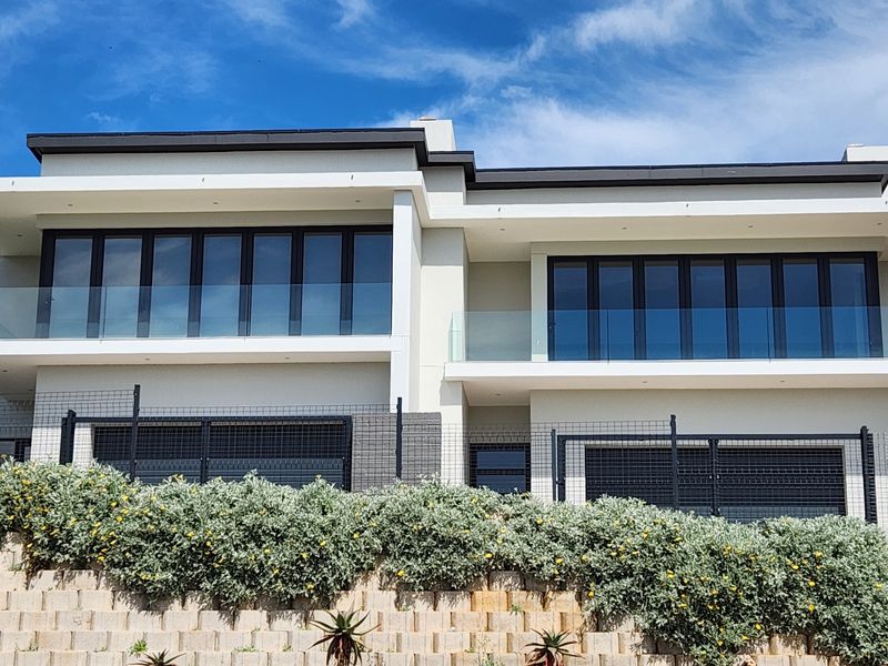 Modern double-story duet property featuring large glass folding doors, glass balustrades on the upper level, and a tiered retaining wall with landscaped garden.