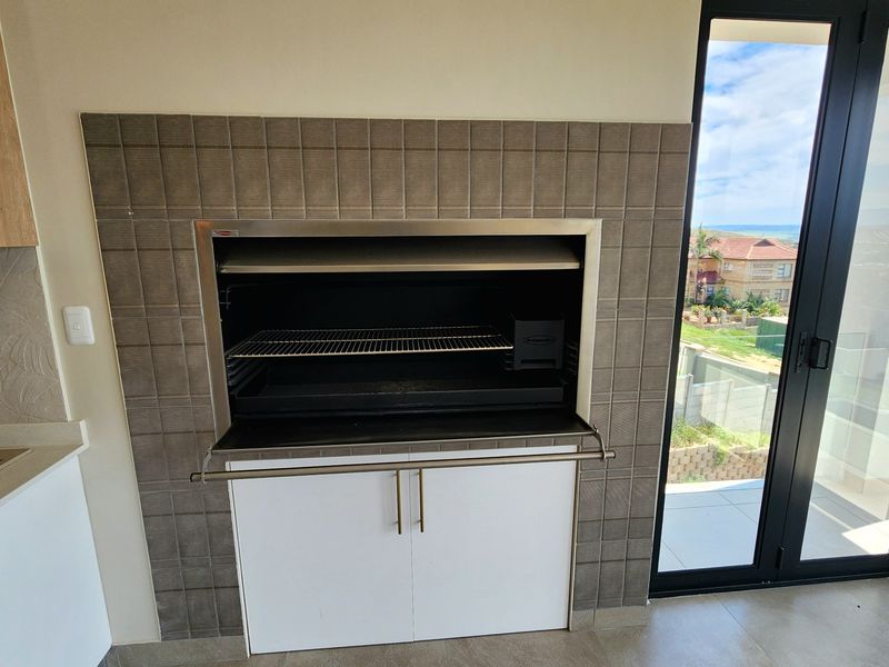 Indoor braai area featuring a built-in stainless steel grill, tiled surround, and adjacent sink, with direct access to an outdoor balcony.
