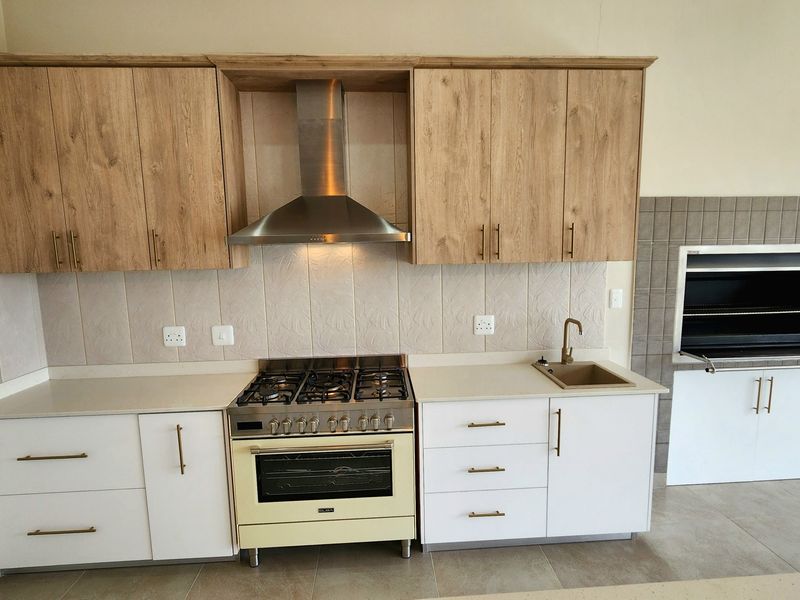 Modern kitchen featuring light wood and white cabinetry, stone countertops, gas stove with extractor, and a built-in indoor braai area.