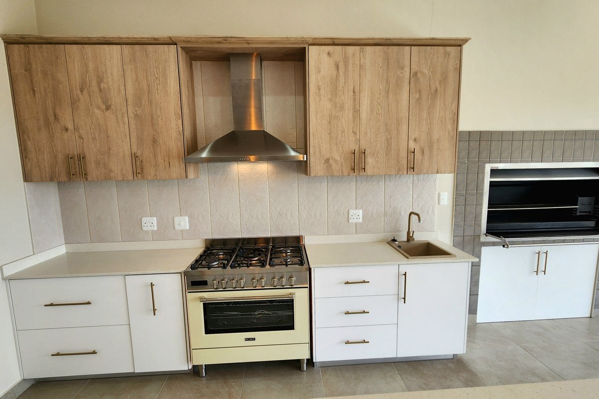 Modern kitchen featuring light wood and white cabinetry, stone countertops, gas stove with extractor, and a built-in indoor braai area.