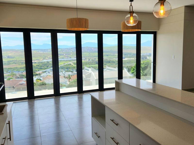Modern open-plan kitchen and living area featuring quartz countertops, built-in braai, and expansive folding glass doors offering panoramic views.