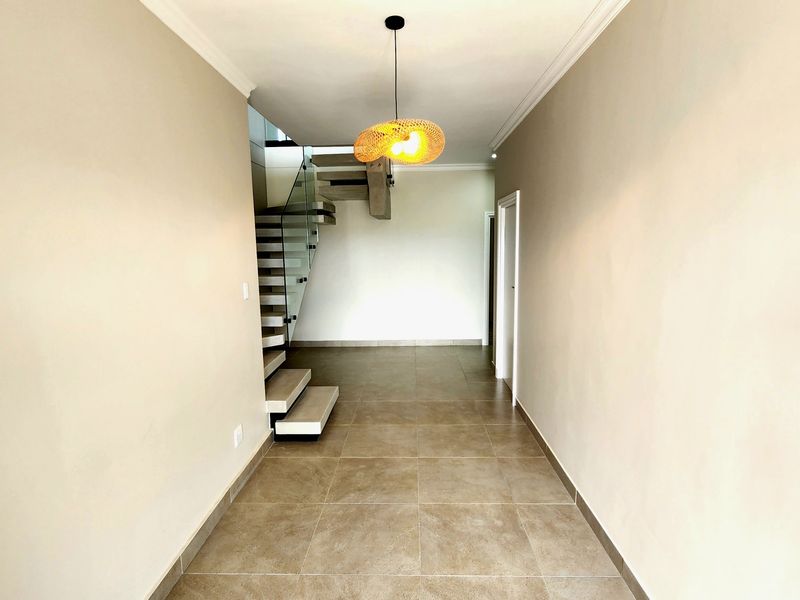 Spacious entrance hallway featuring modern tiled flooring and a contemporary floating staircase with a glass balustrade.